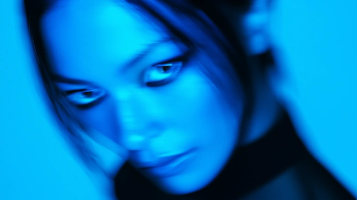 Close-up portrait of a woman with a blurred, blue-toned effect and downcast eyes.