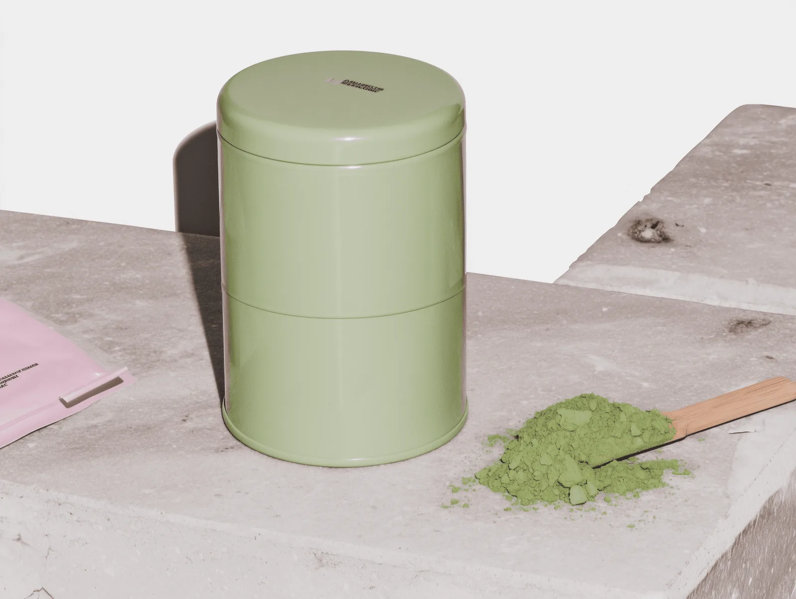 Green matcha tin with a wooden scoop on a stone surface