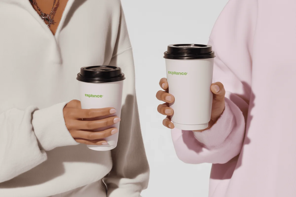 Hands holding two takeaway matcha drinks against a soft neutral background